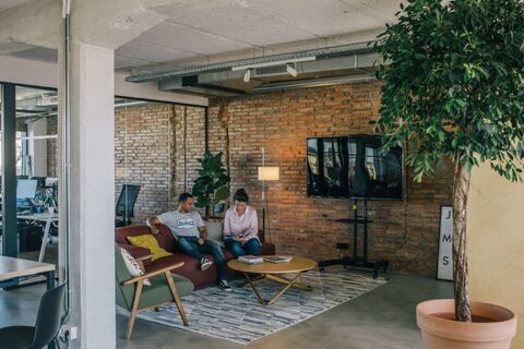 a man and woman sitting on a couch in a room with brick walls