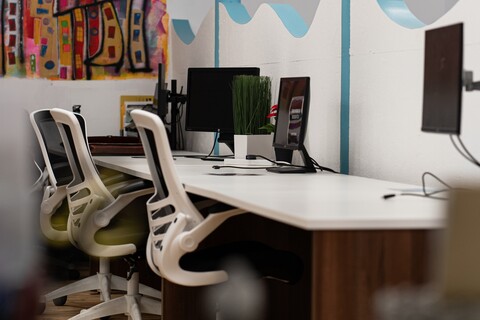 a desk with computers and chairs in front of a wall