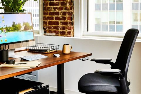 a desk with a computer and a chair in front of a window