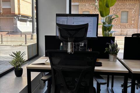 a desk with computer and plant in front of a window